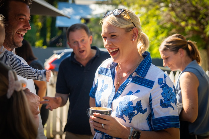 A smiling woman holds a coffee with people around her