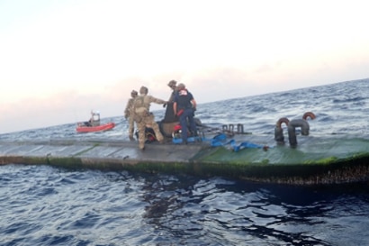 People in uniforms stand on a long, narrow, low-profile vessel at sea.