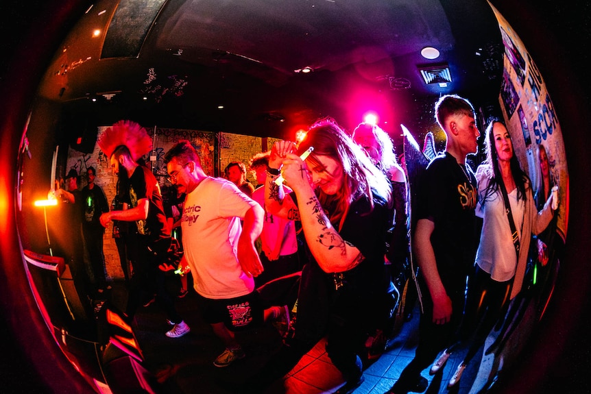 A fish eye photograph of men and women in the audience at a Wicked Envy concert dancing.