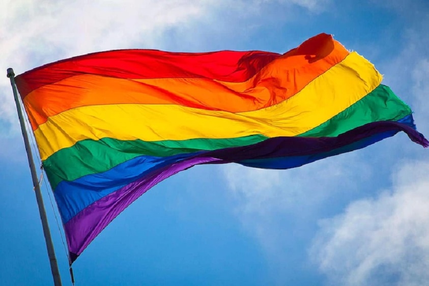 A flag with the colours of the rainbow flying on a flag post.