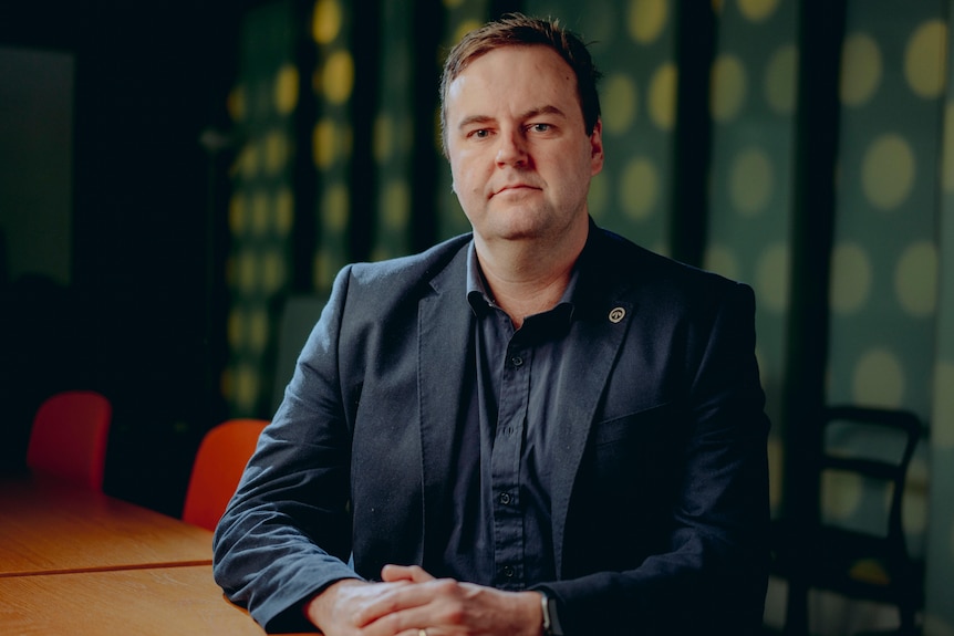 Toby Warnes RTBU NSW Secretary sits at a desk with his hands folded on the table