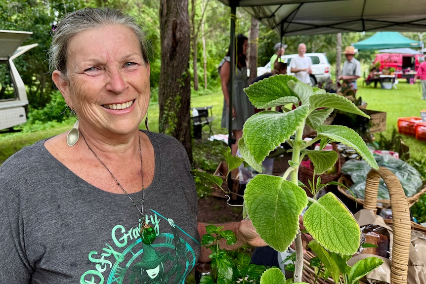 A smiling woman holding up herbs at a farmers market stall.