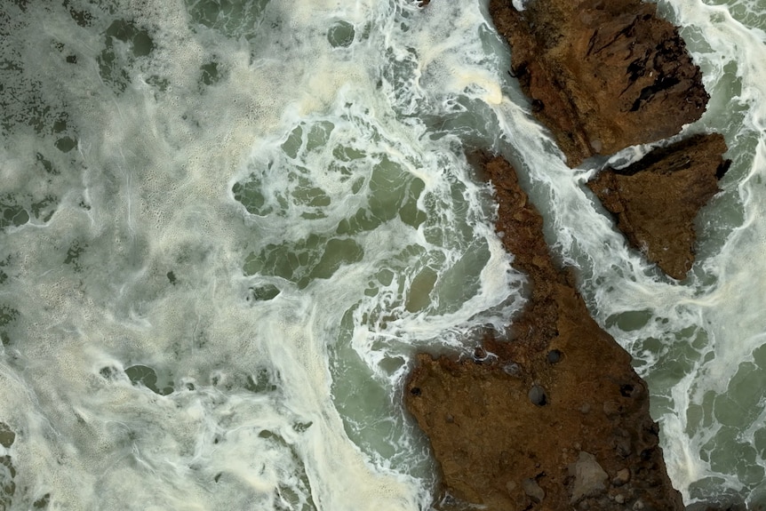 White foam on top of green water. The foam is being swirled by the movement of the ocean hitting rocks.