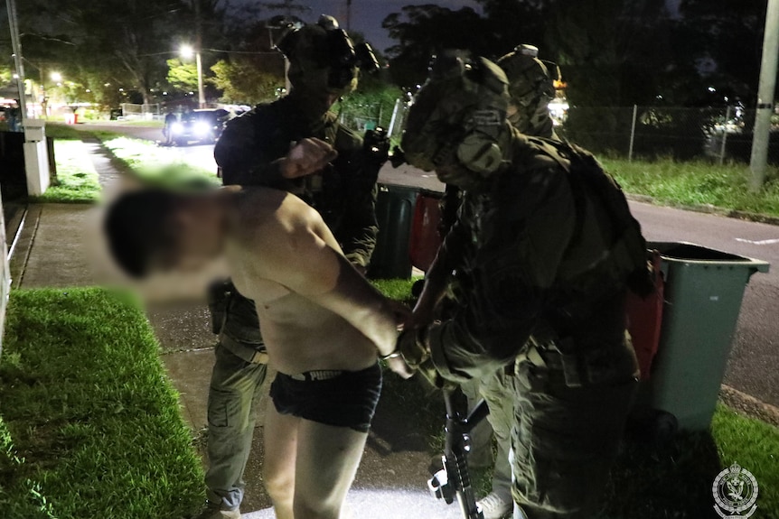 three police officers in helmets and in dark put handcuffs in man in underpants