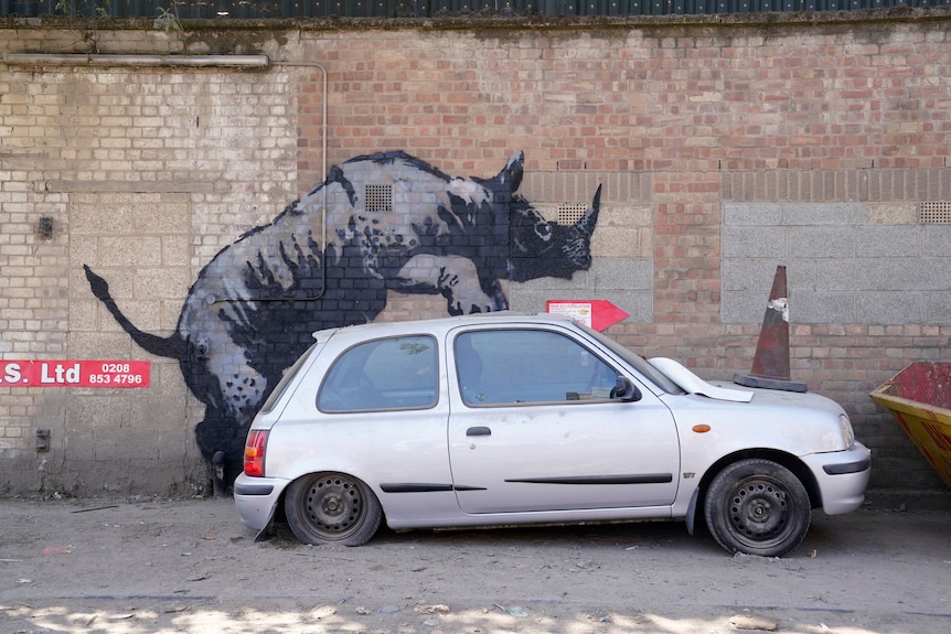 A mural of a rhino, which appears to show the animal mounting a broken-down car