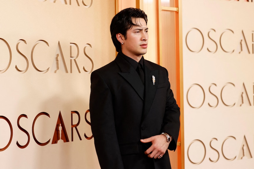 Hudson wiliams in a dark suit wtih a brooch and bracelet.