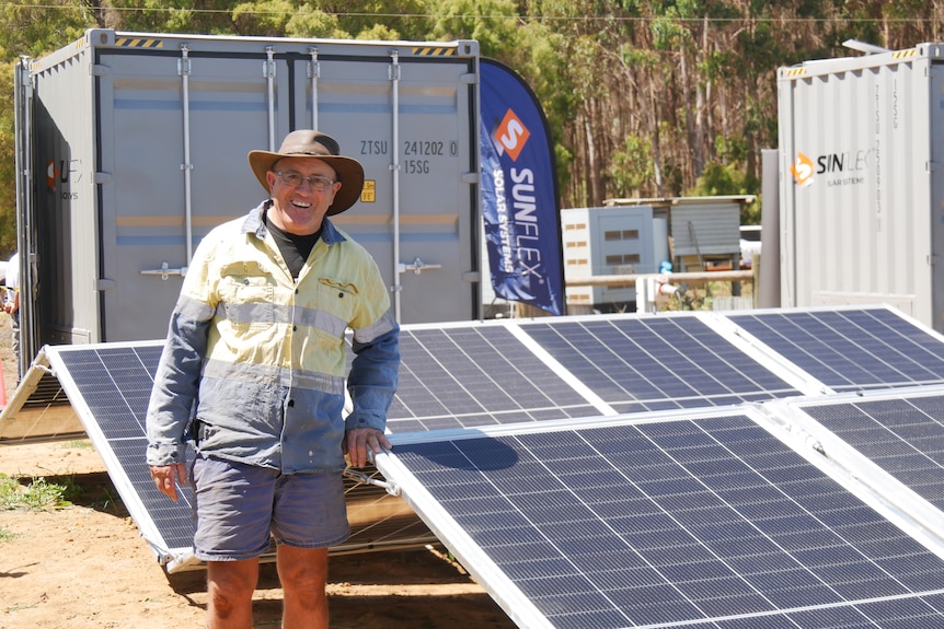 Man in long-sleeved shirt standing next to solar panels.