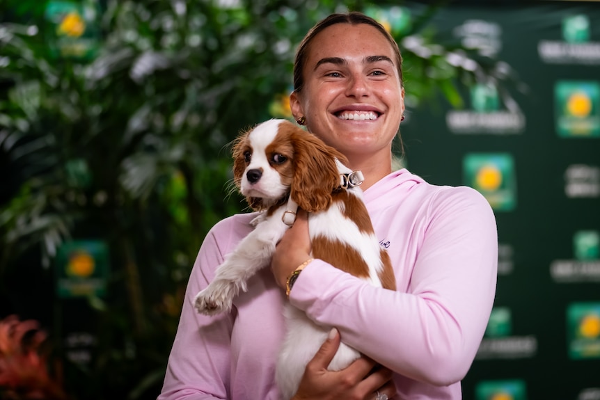Aryna Sabalenka smiles and holds her pet puppy dog