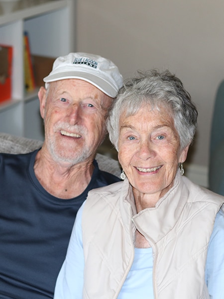 An elderly couple on a couch smiling for the camera.