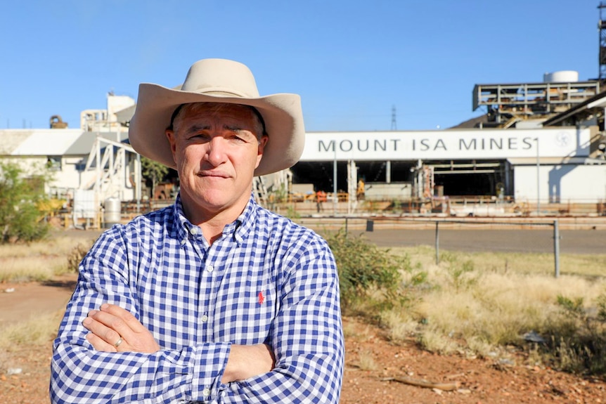 a man in a hat crosses his arms in front of mount isa mines.