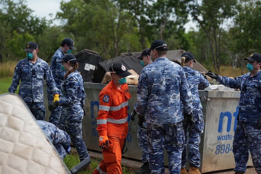 A group of Air Force members in unifrom wearing masks next to skip bin with SES volunteer in middle of group