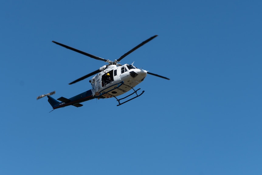 Blue and white helicopter flying against blue sky