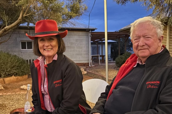 A couple smiling at the camera wearing black jackets, the woman has a red cowboy style hat