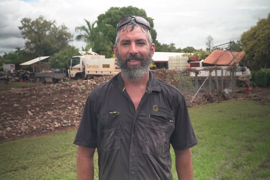 A man in a work shirt standing out the front of his flood-damaged home.