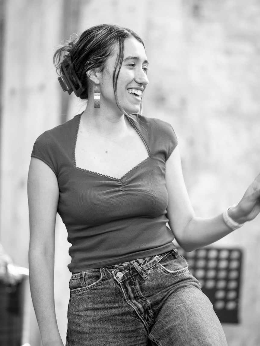 A black and white photo of Margaret Thanos, smiling and wearing a t-shirt and jeans.