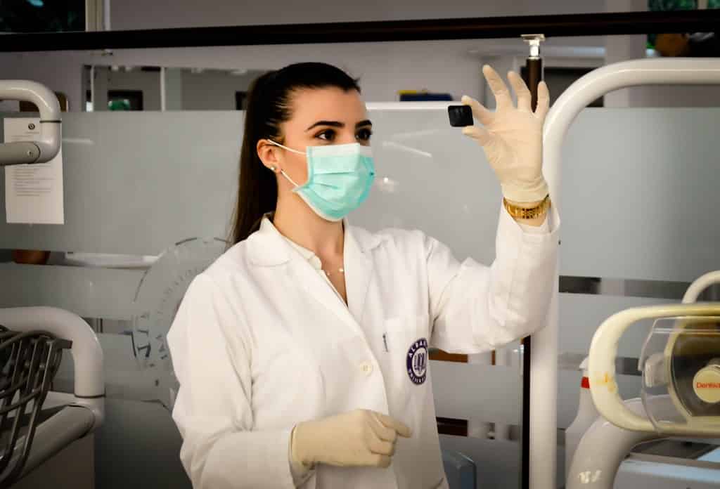 Female scientist wearing a mask and gloves examining a sample in a modern laboratory for scientific research.