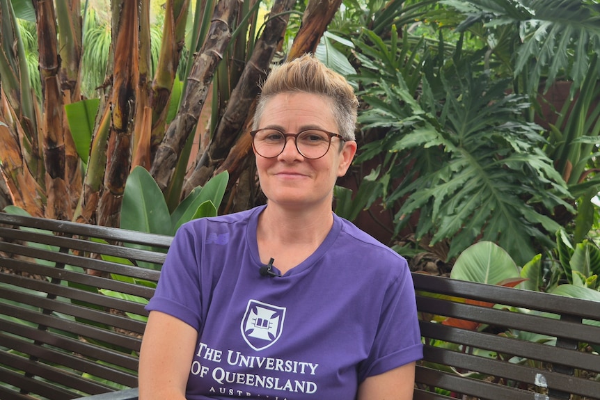 A woman in a university of queensland shirt sits on a bench