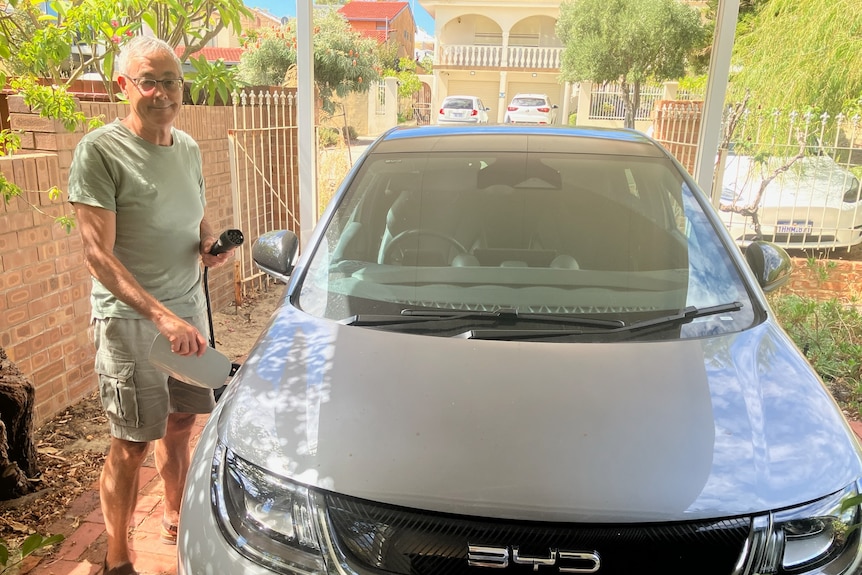 a man with grey hair standing in a carport holding an EV charger to his car