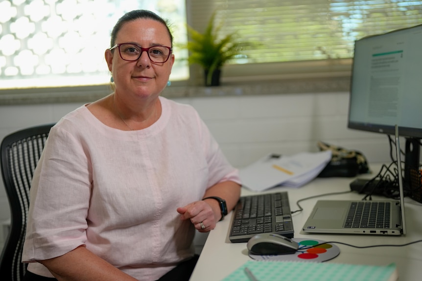 A woman sitting at a desk and smiling at a camera. 