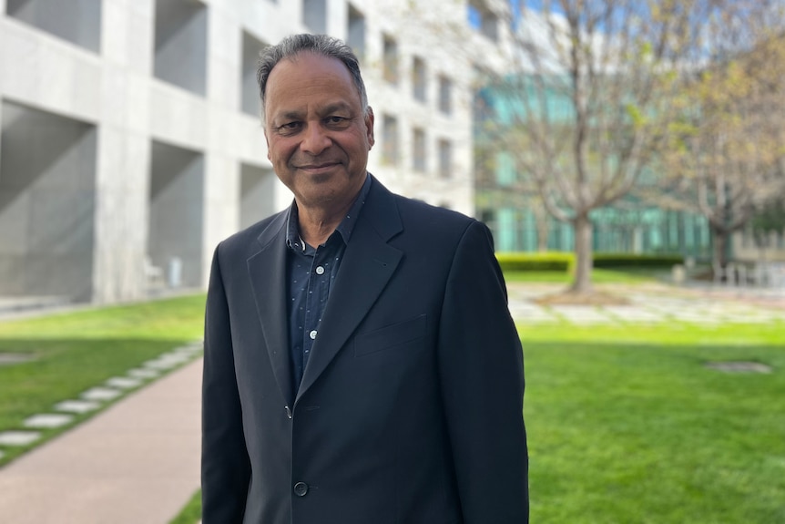 Rizvi stands in a parliament courtyard smiling.
