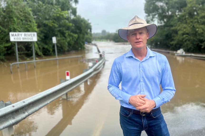 Glen in a hat standing in front of a flooded bridge.
