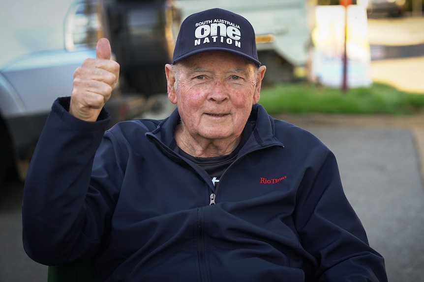 An elderly man in a wheelchair with a One Nation holding a thumbs up