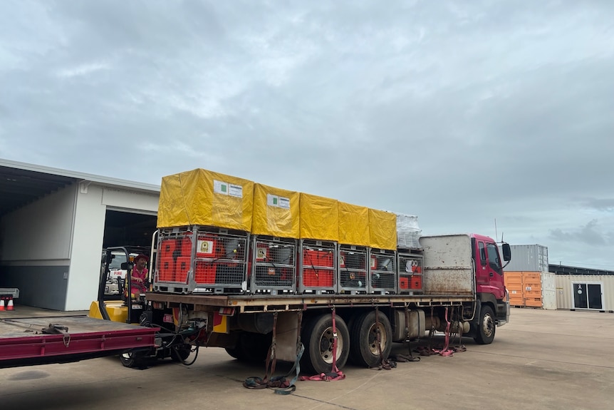 A truck with multiple crates on the tray with yellow tarps on them.