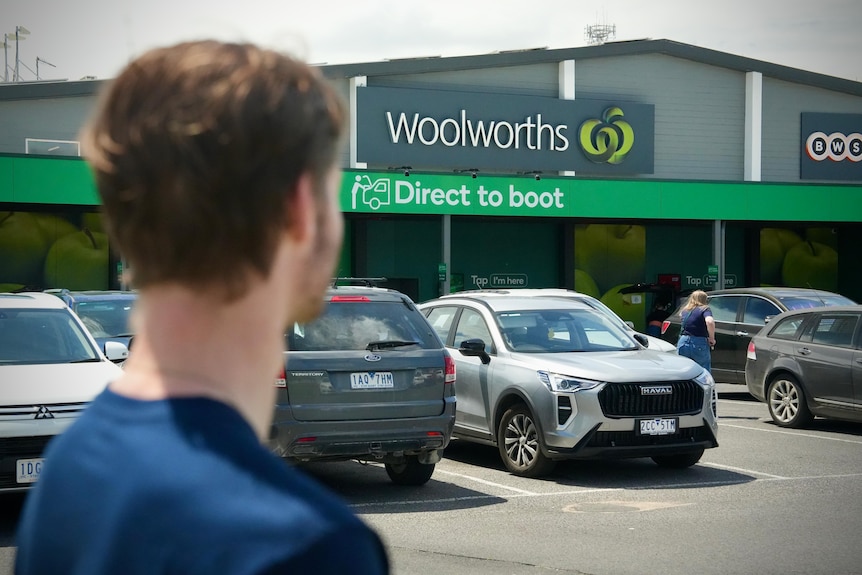 The back of a young man's head, as he stands in a Woolworths supermarket carpark.