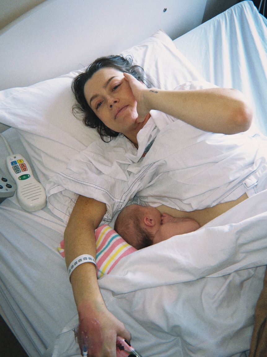 Madeleine Edwards lying reclined on the white linen of a hospital bed while breastfeeding.