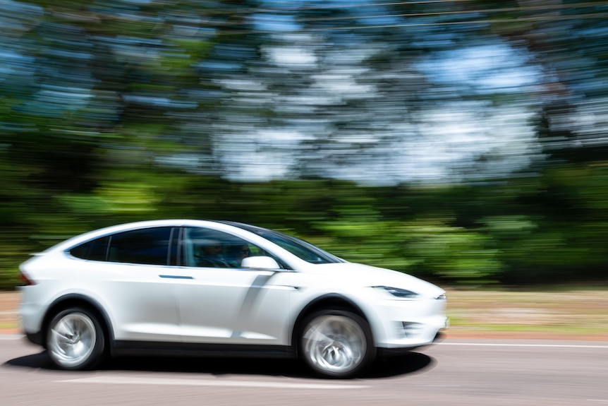 A white car drives fast on a Darwin road.
