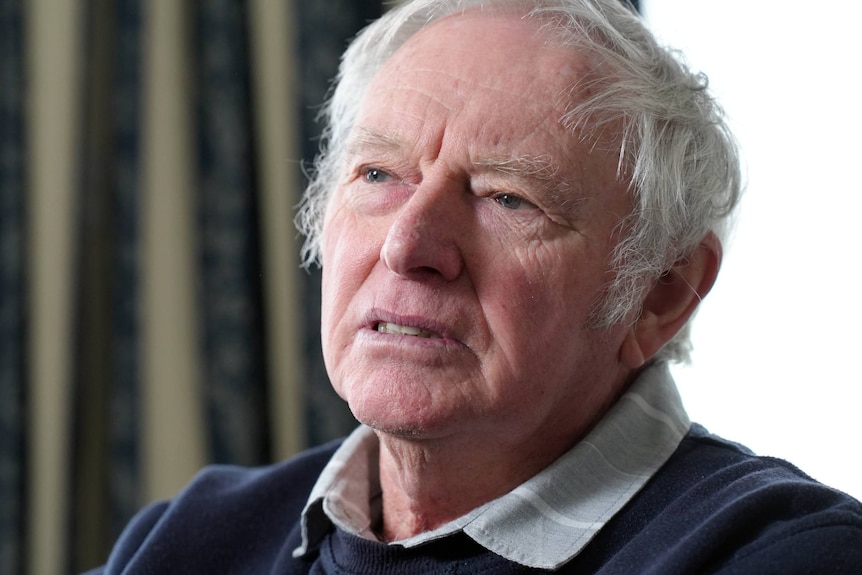 Grey haired man wearing a blue jumper looking away from the camera.