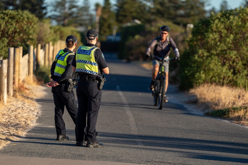 two police officers on a bike path looking at an oncoming cyclist