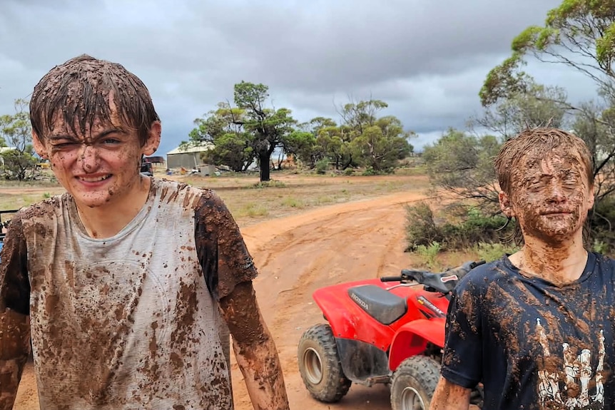 Two boys covered in mud on a farm.