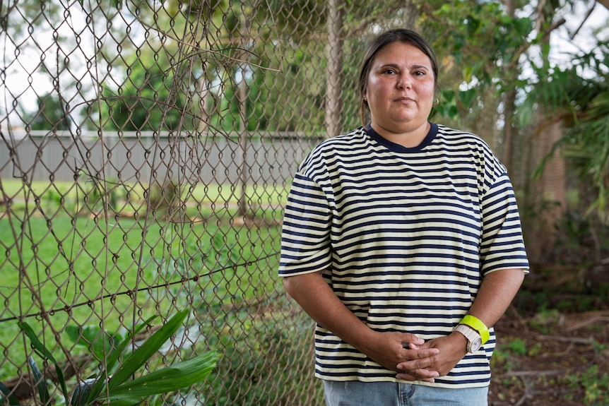 A woman in a striped shirt standing next to a chain link fence