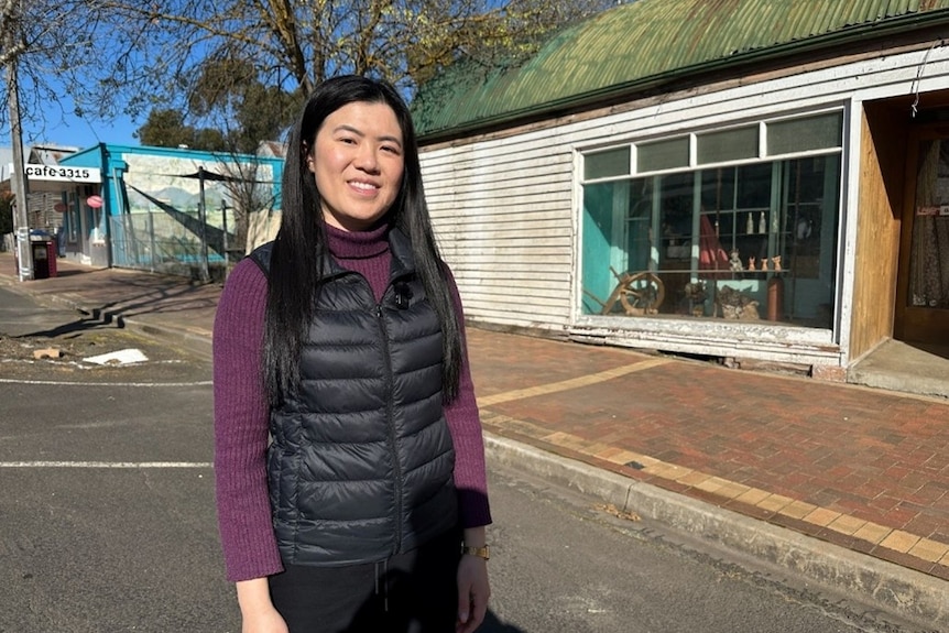 Annie Louey stands in a street with a wooden shopfront with a large window behind her