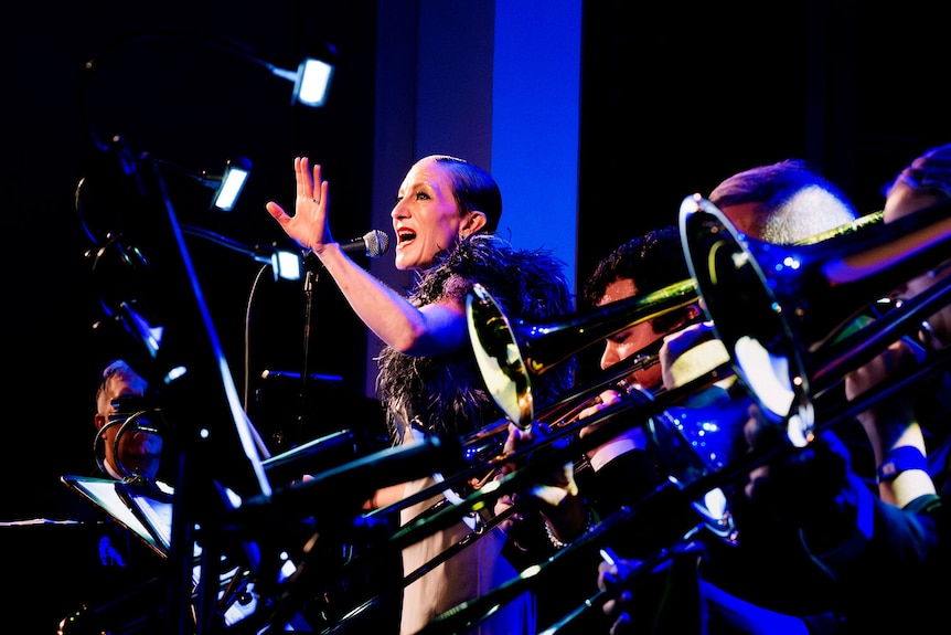 Woman singing at microphone on stage, surrounded by brass band
