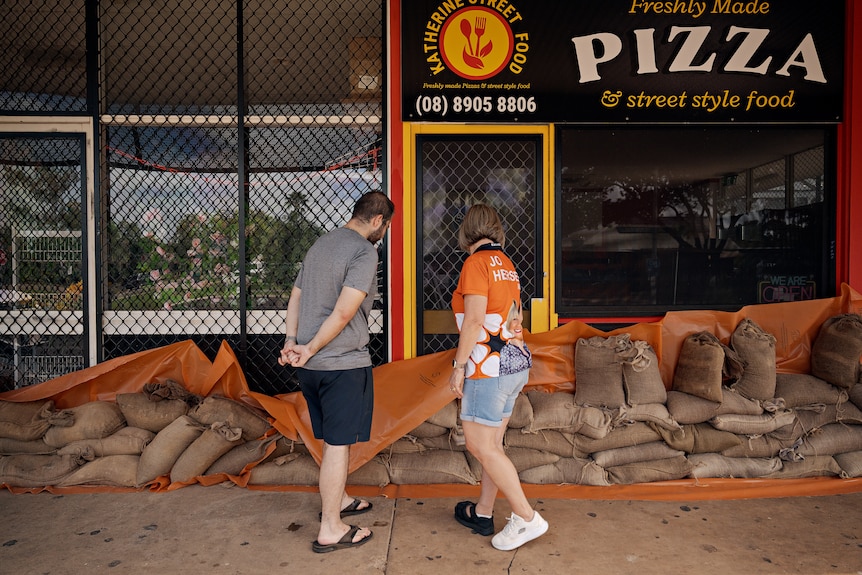 A man and woman look at sandbags piled up at a business door.