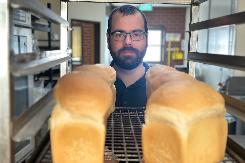 A man with his head next to several loafs of breads.