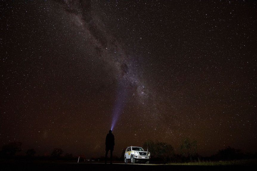 A stargazer points a torch at the night sky.
