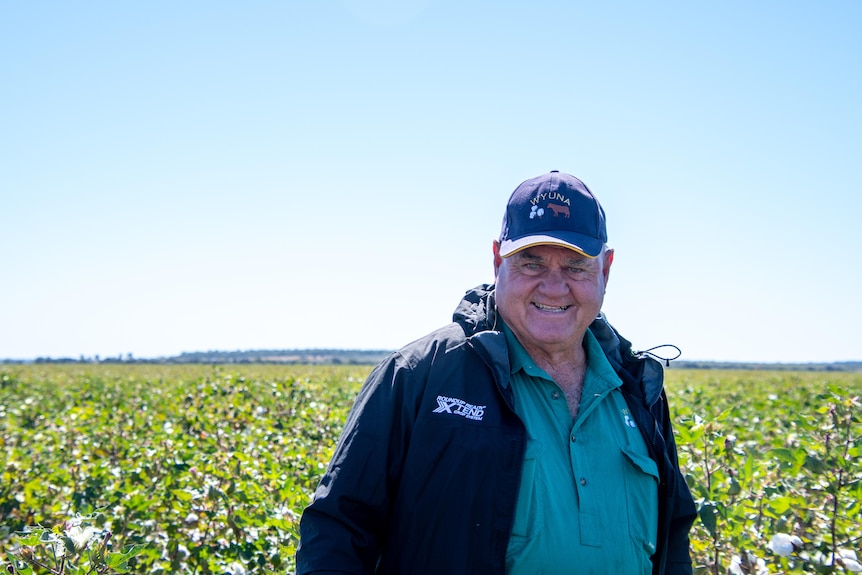 Farmer Ian Burnett smiles in front of a field of cotton crops. 