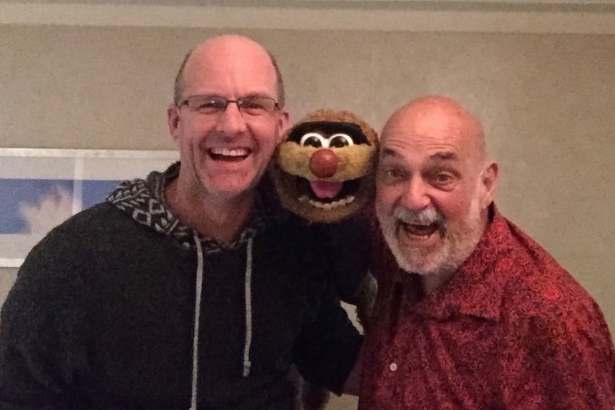 Two men smiling at the camera with Agro the puppet between them