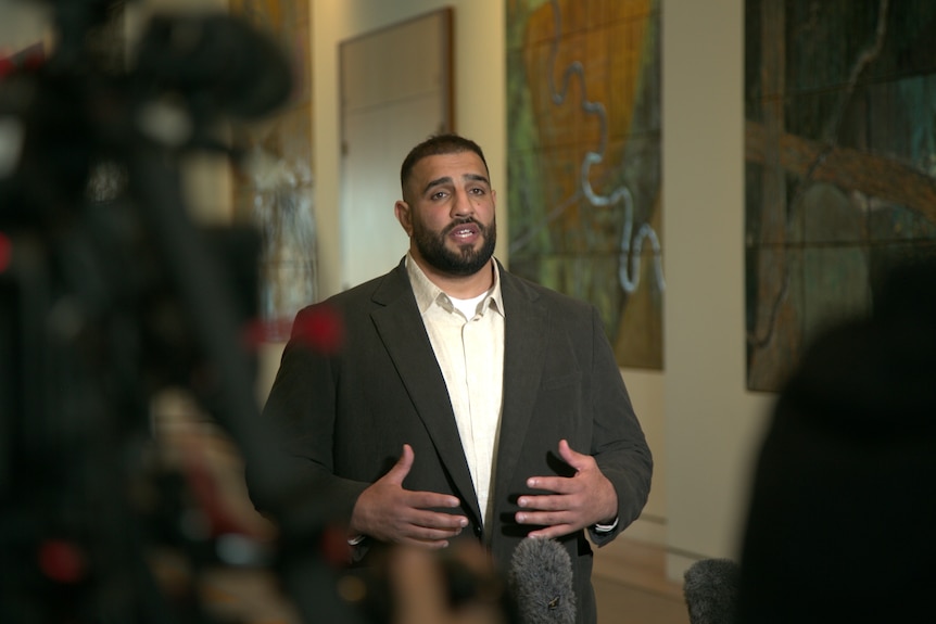 A man in a suit speaks to a media scrum