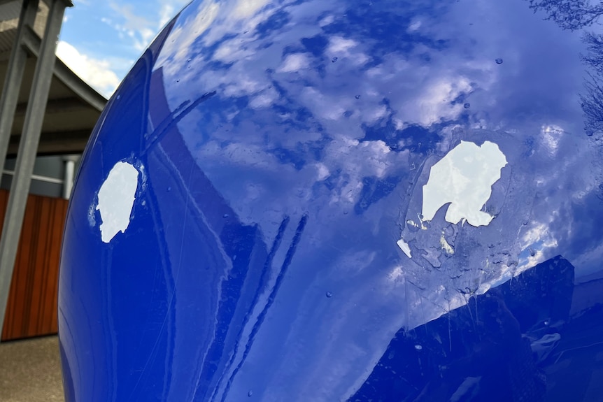 Large white marks in the shape of eyes on a large blue sculpture.