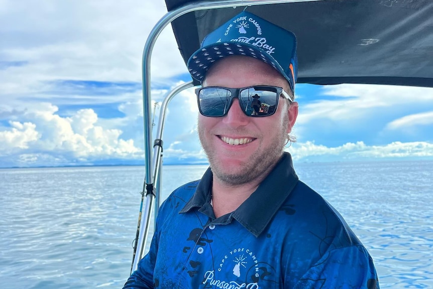 Jack Colquhoun wears a blue shirt and holds a fishing road, on a boat.