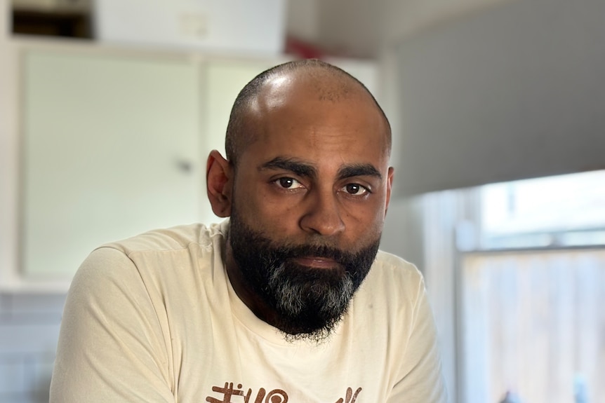 An Indigenous man looks at the camera in a kitchen.
