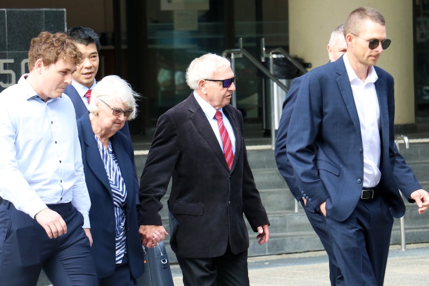 Barry Cable holds his wife's hand and is surrounded by supporters as he walks outside court