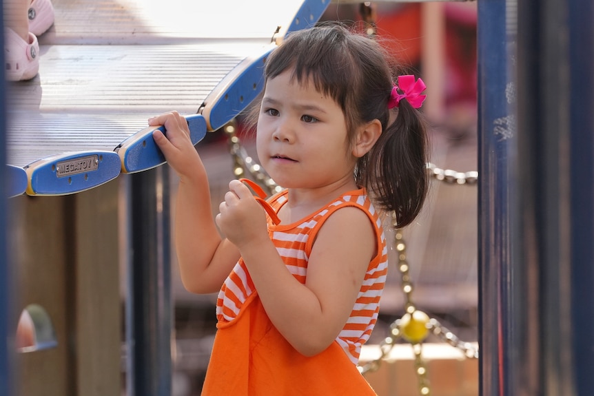 A young girl with black pigtails stands on a playground.