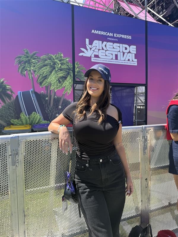 A young woman in black clothing poses against a mesh barricade.