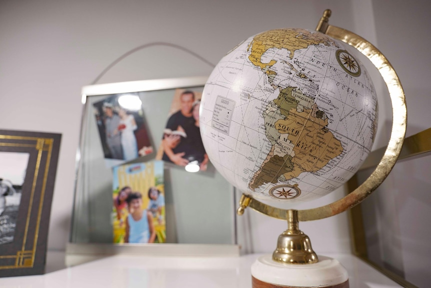 A globe in the foreground, focussed on South America, and a glass pane in the background covered with photos of family.