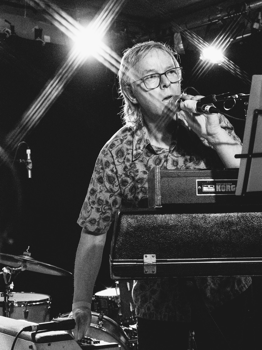 Black and white photo of man standing at microphone on stage performing.